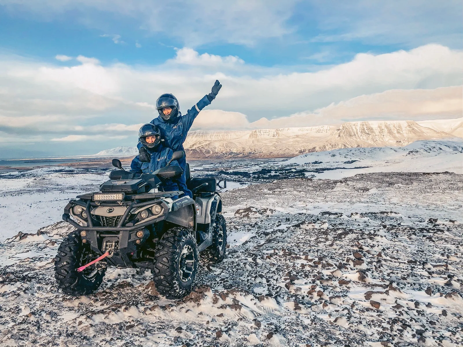 Tveir fjórhjólafarþegar fagna á fjallstindi með útsýni yfir snævi þakin fjöll
