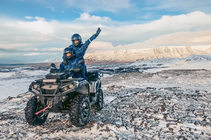 Tveir fjórhjólafarþegar fagna á fjallstindi með útsýni yfir snævi þakin fjöll