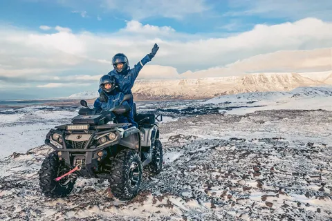 Tveir fjórhjólafarþegar fagna á fjallstindi með útsýni yfir snævi þakin fjöll